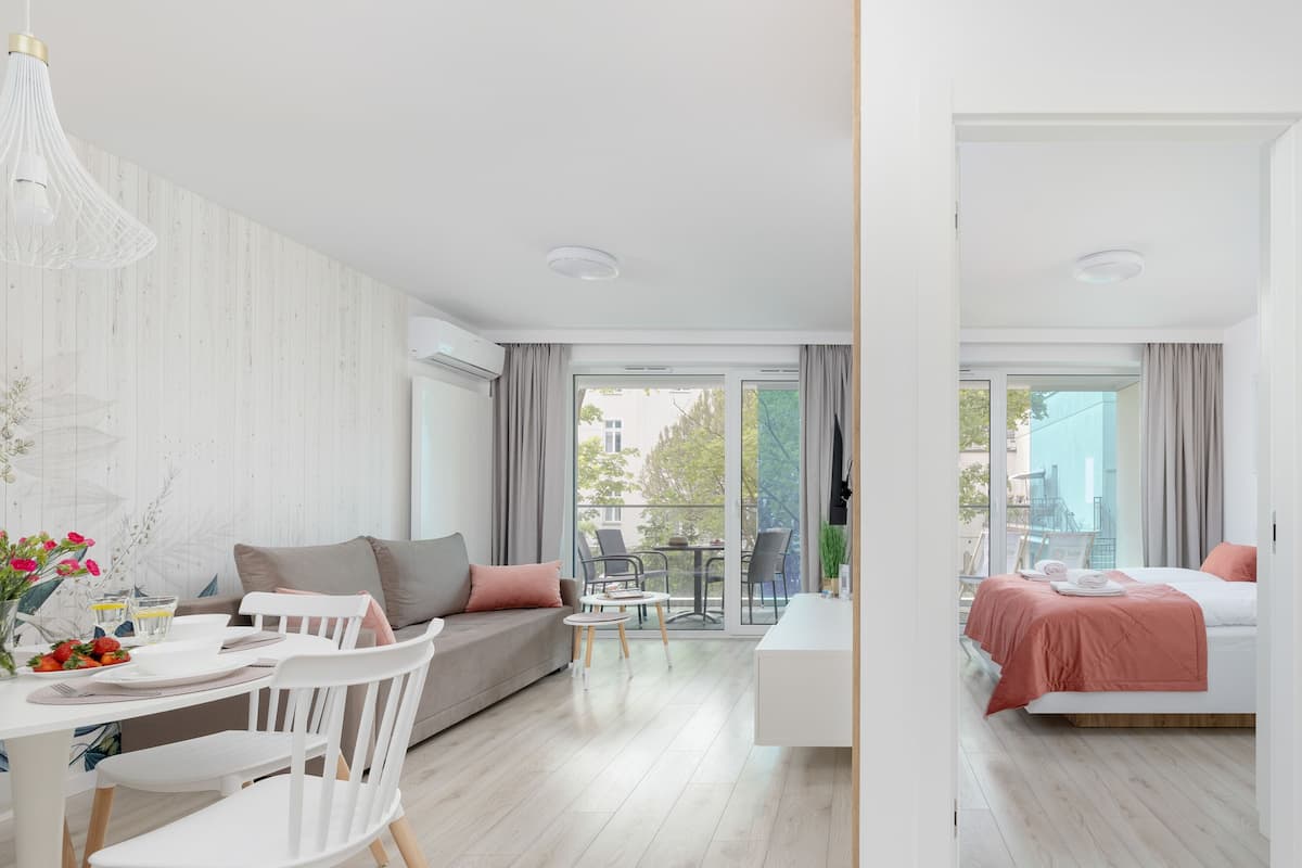 Ett modernt hotellrum med en balkong, en matplats och en säng med ett rosa överkast.