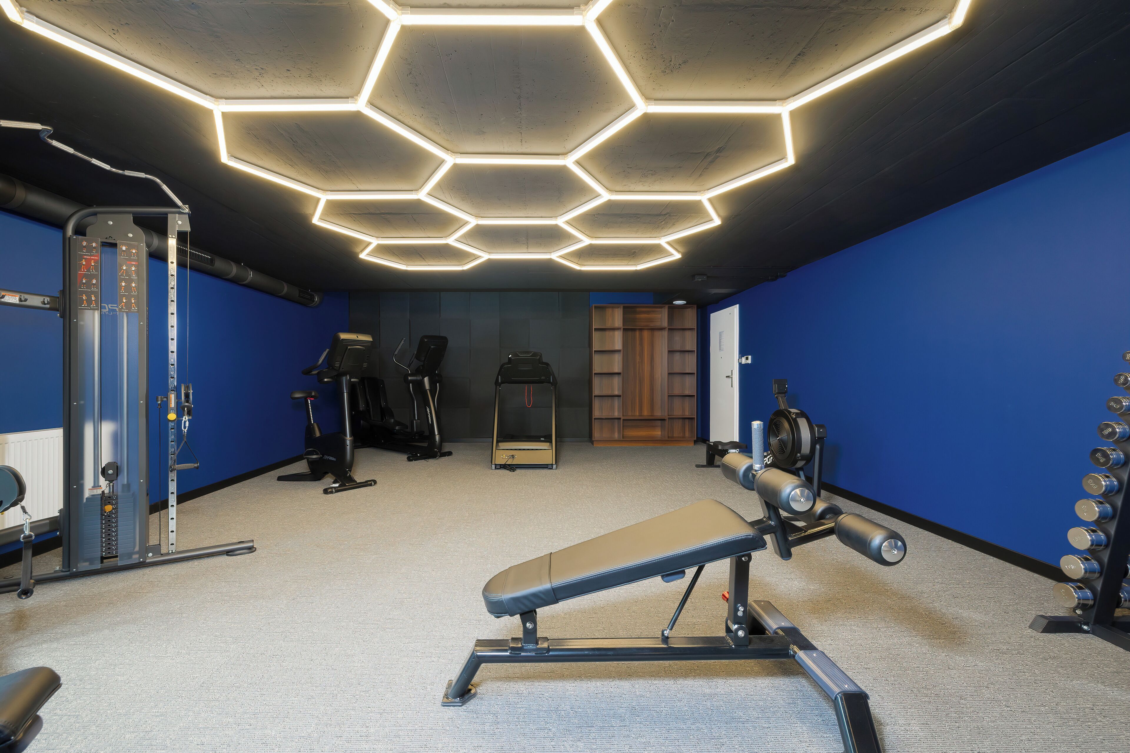 A gym with hexagonal ceiling lights, exercise equipment, and blue walls.