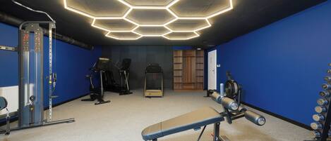 A gym with hexagonal ceiling lights, exercise equipment, and blue walls.