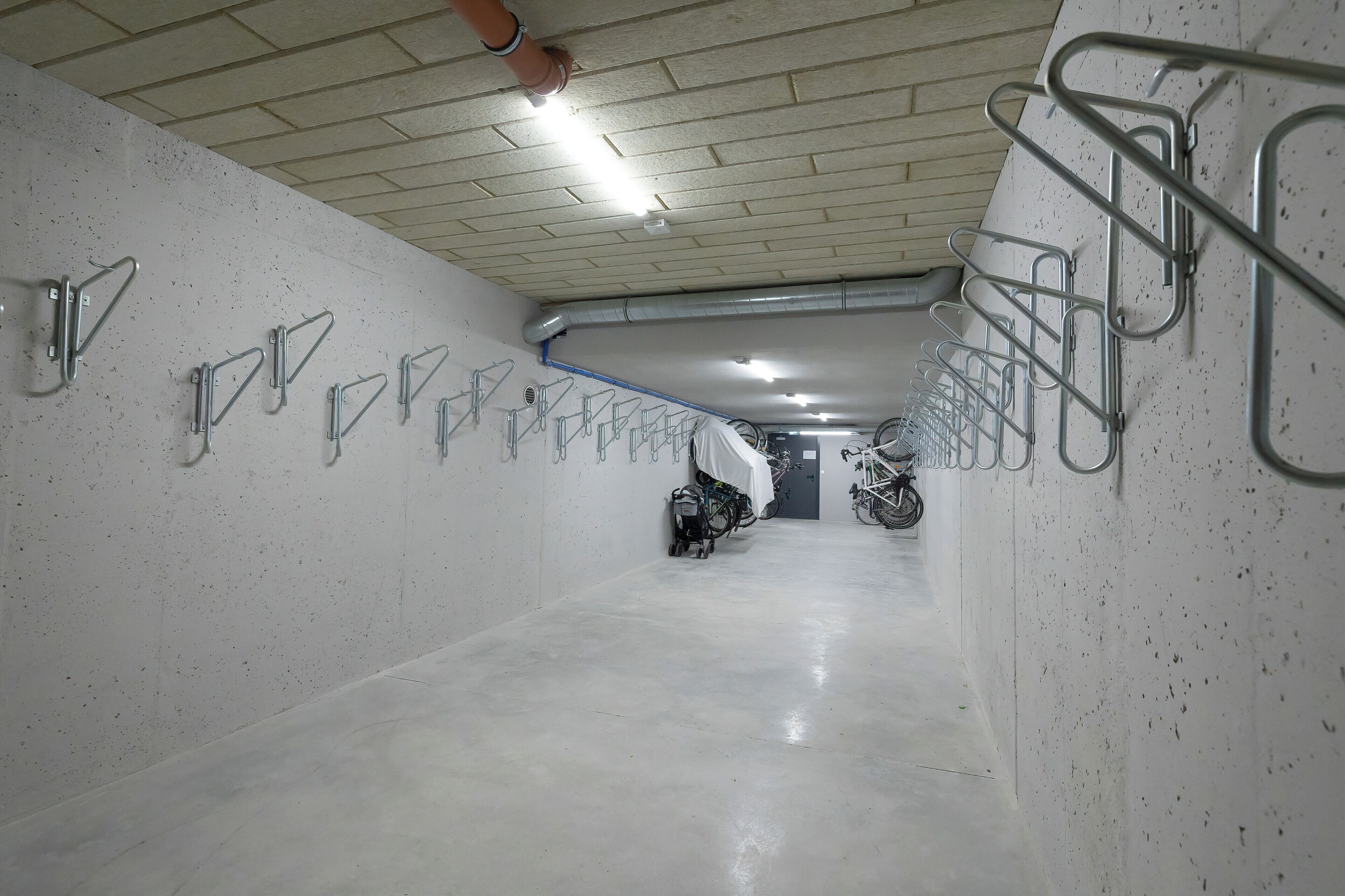 Ein sauberer, gut beleuchteter Innenraum mit Fahrradständern an den Wänden und einem Betonboden.