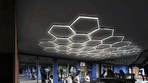 Uma academia moderna com luminárias hexagonais no teto, equipamentos de ginástica e grandes espelhos.