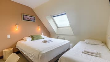 A bedroom with two beds, a skylight, a painting, and a small stool.