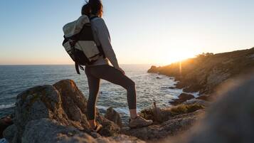 A person standing on a rocky outcrop overlooking the ocean at sunset.