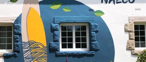 Un edificio con un mural de una tabla de surf y la palabra "NAECO" en la fachada.
