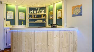 A reception desk with a wooden panel design, a sign reading "NAÉCO", and framed informational posters on the wall.