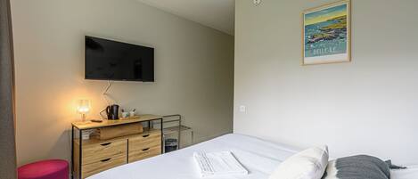 A hotel room with a bed, a desk with a lamp, a flat-screen TV, a wooden dresser, and a framed picture on the wall.