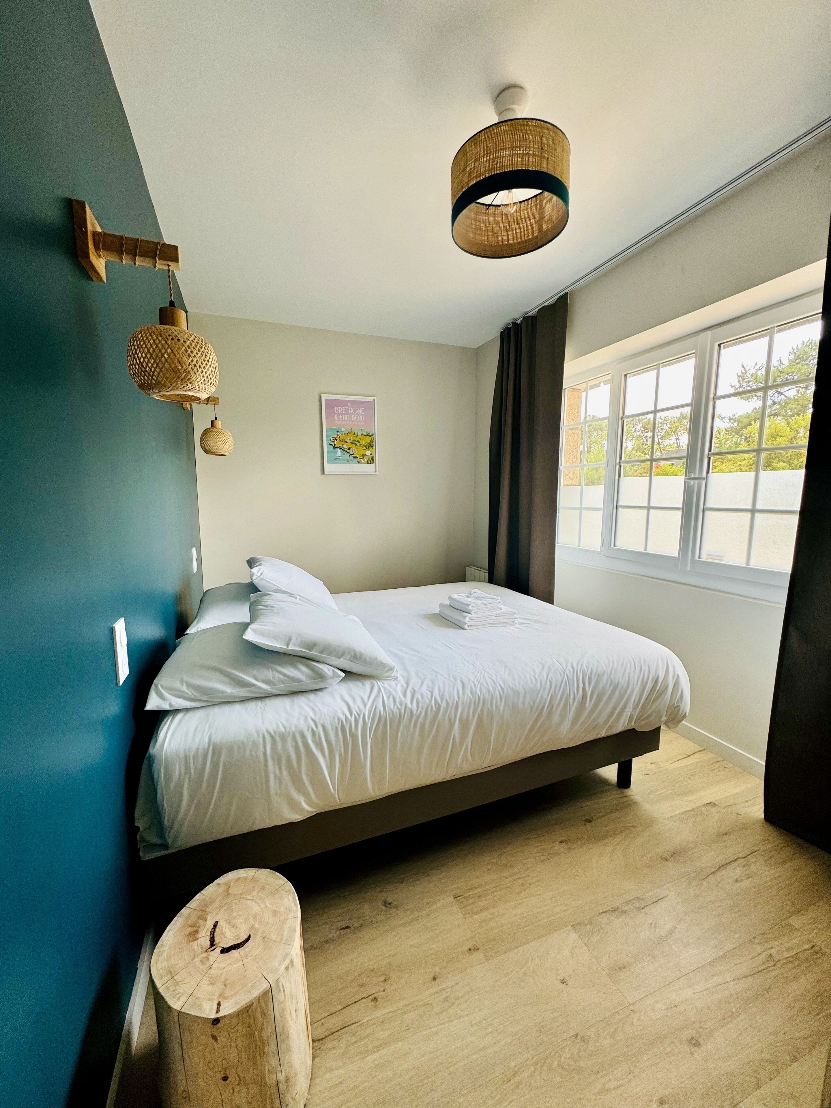 Une chambre à coucher avec un lit, un plancher en bois, une fenêtre et un luminaire fixé au mur.
