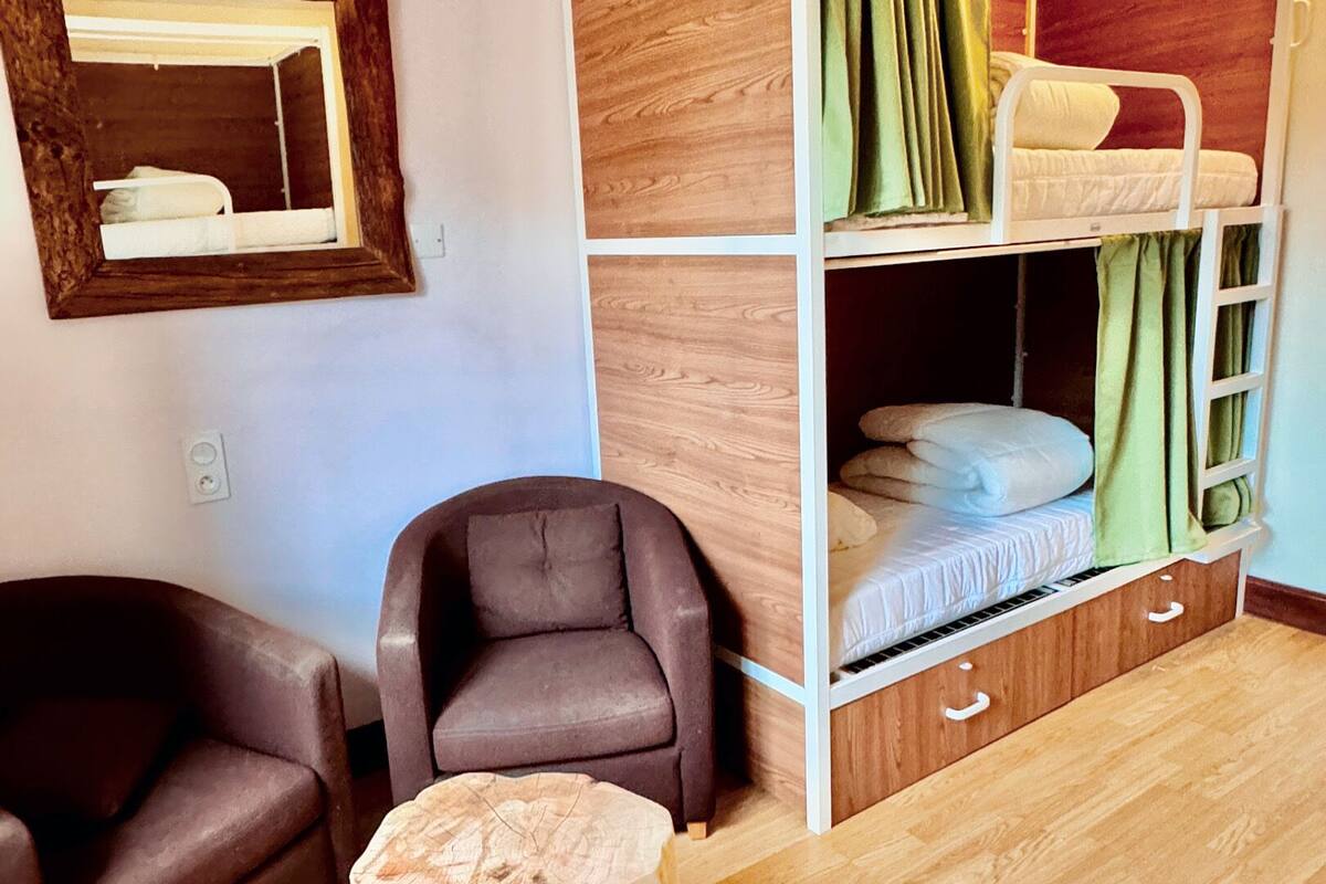 Une pièce avec un lit superposé, une chaise, une petite table et un miroir au mur.