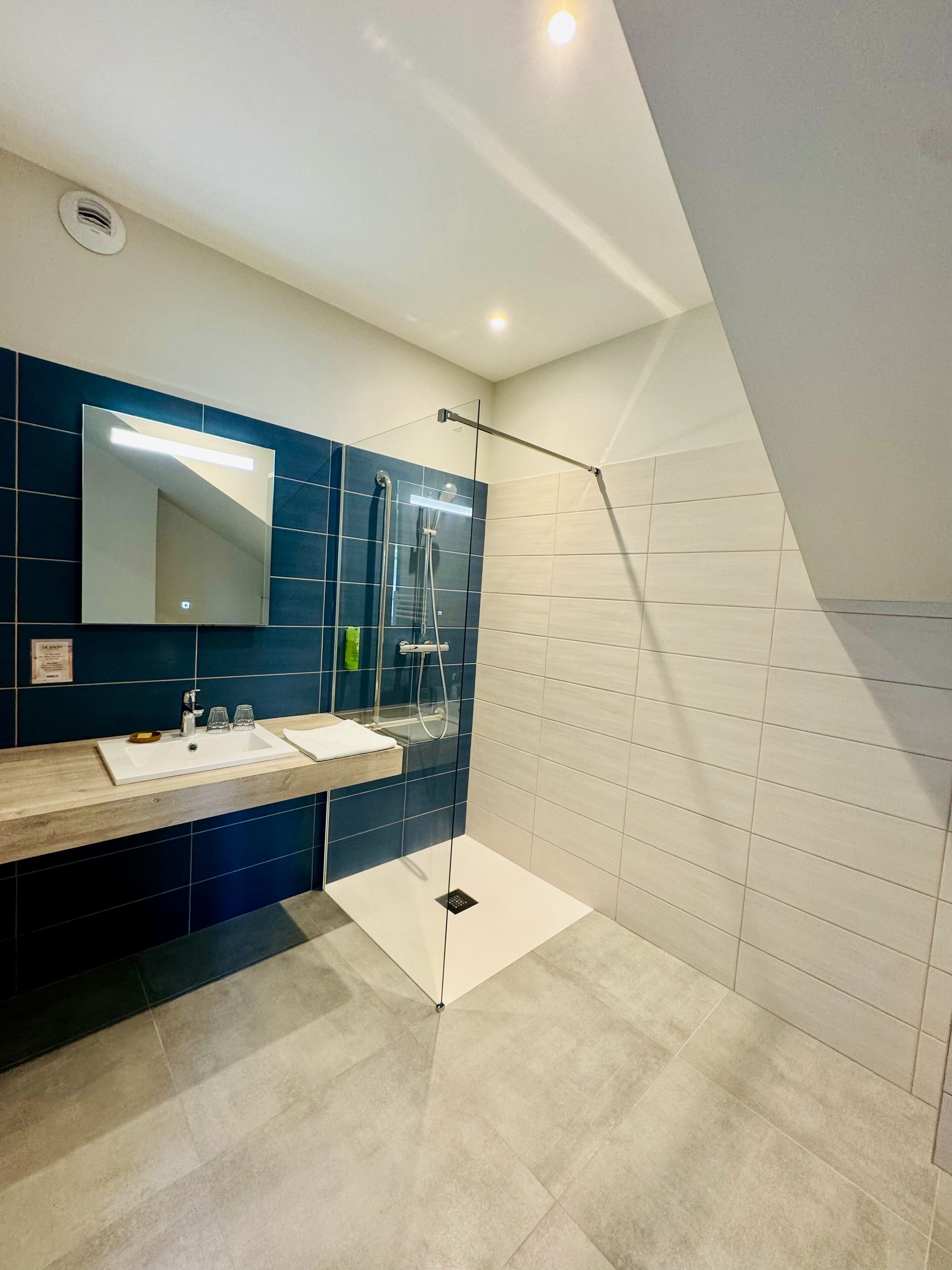 A modern bathroom with a large mirror, two sinks, a shower, and a tiled floor.