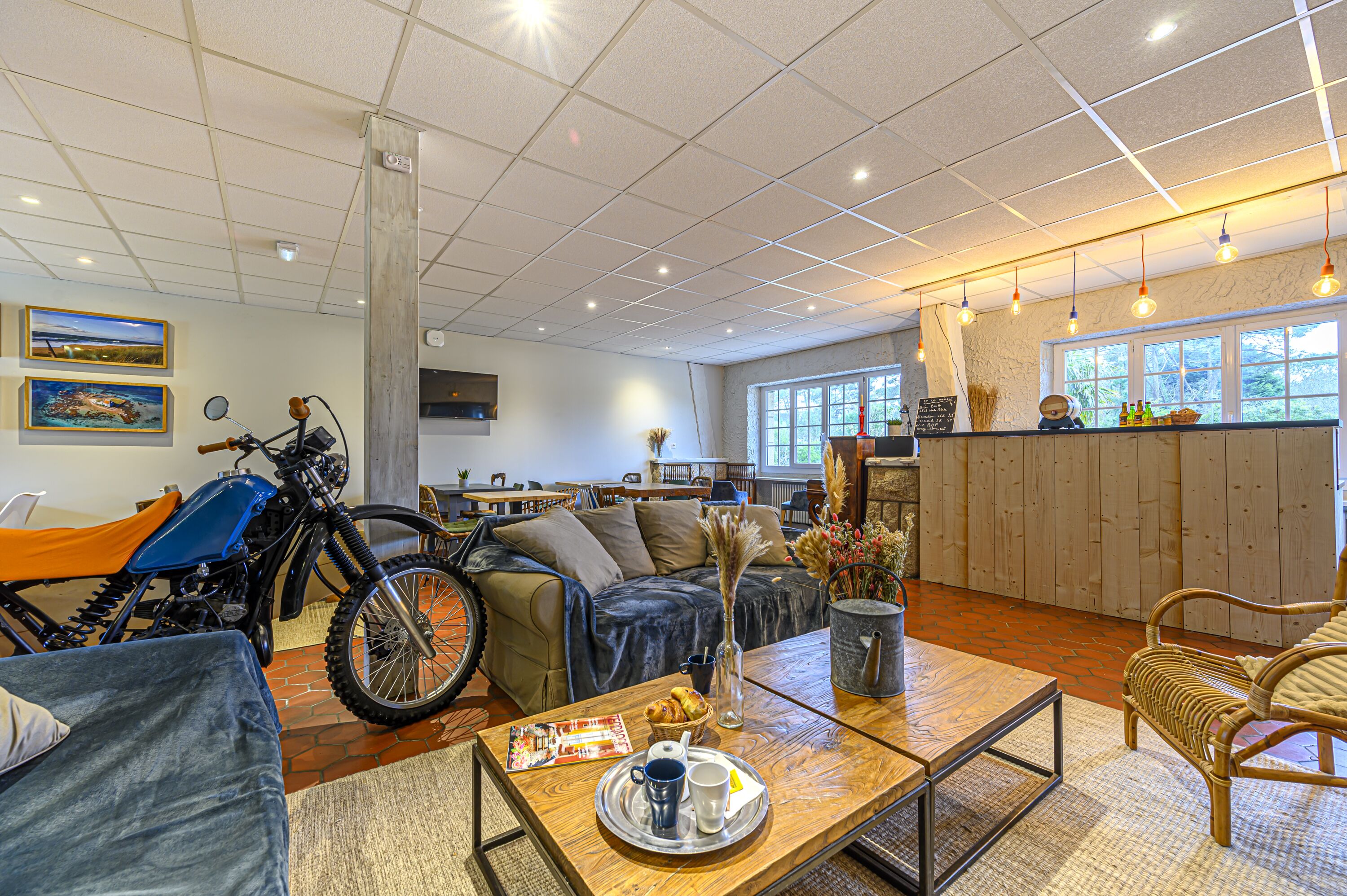 Een ruime woonkamer met een motor, een bank, een bijzettafeltje met dienblad en uitzicht op het omliggende landschap door grote ramen.