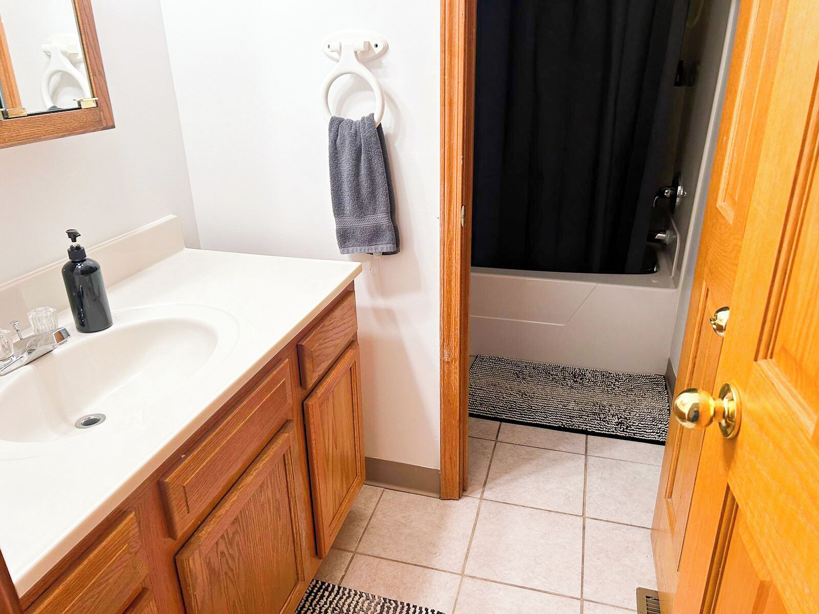 A bathroom with a white sink, wooden cabinets, a towel rack with a towel, a black shower curtain, and a wooden door.