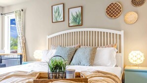 Una cama bien hecha con una bandeja de madera, almohadas y una pequeña planta. Hay obras de arte en la pared y una lámpara en la mesita de noche.