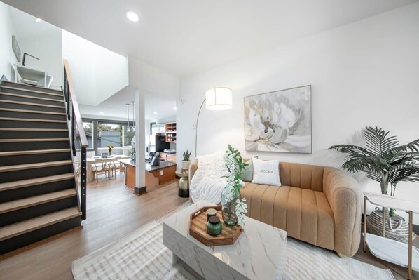 A modern living room with a staircase, a sofa, a coffee table, and a painting on the wall.