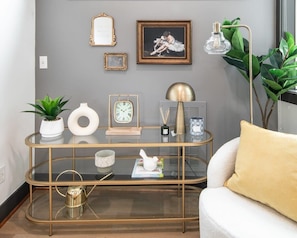 Ein modernes Wohnzimmer mit einem Glastisch, einem weißen Sofa und einer Uhr mit goldener Rahmen.
