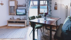 Um quarto acolhedor com uma mesa de jantar de madeira, cadeiras verdes, uma televisão e uma janela com cortinas.