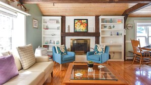 A cozy living room with a fireplace, blue armchairs, a glass coffee table, and wooden floors. - Private Pool, Large Deck, and Game Room! (Dennis)