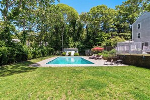 A rectangular swimming pool with a paved deck, surrounded by a grassy lawn and trees. - Private Pool, Large Deck, and Game Room! (Dennis)