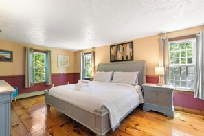 Una habitació d'hotel amb un llit, taules de nit, una finestra amb cortines, un quadre a la paret i vistes a la vegetació exterior.