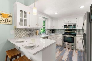 Une cuisine moderne avec des meubles blancs, un îlot central doté de deux éviers, un four en acier inoxydable et un four à micro-ondes.