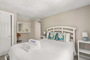 A hotel room with a bed, two pillows, a nightstand, a lamp, a mirror, and a towel.