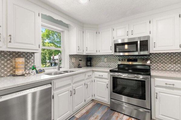 A modern kitchen with white cabinetry, stainless steel appliances, and a patterned backsplash. - Private Pool, Large Deck, and Game Room! (Dennis)