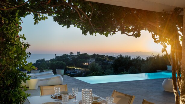 A dining table set for four with a view of a pool and landscape. - New property_Sa Turri: Relax, Infinity Pool, Seaview, enchanting Sunsets (Torre Delle Stelle (Maracalagonis))