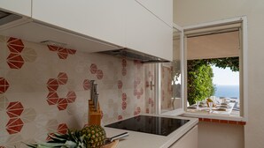 A kitchen with a modern design, featuring a geometric patterned backsplash, a built-in stove, and a window overlooking a scenic view. - New property_Sa Turri: Relax, Infinity Pool, Seaview, enchanting Sunsets (Torre Delle Stelle (Maracalagonis))