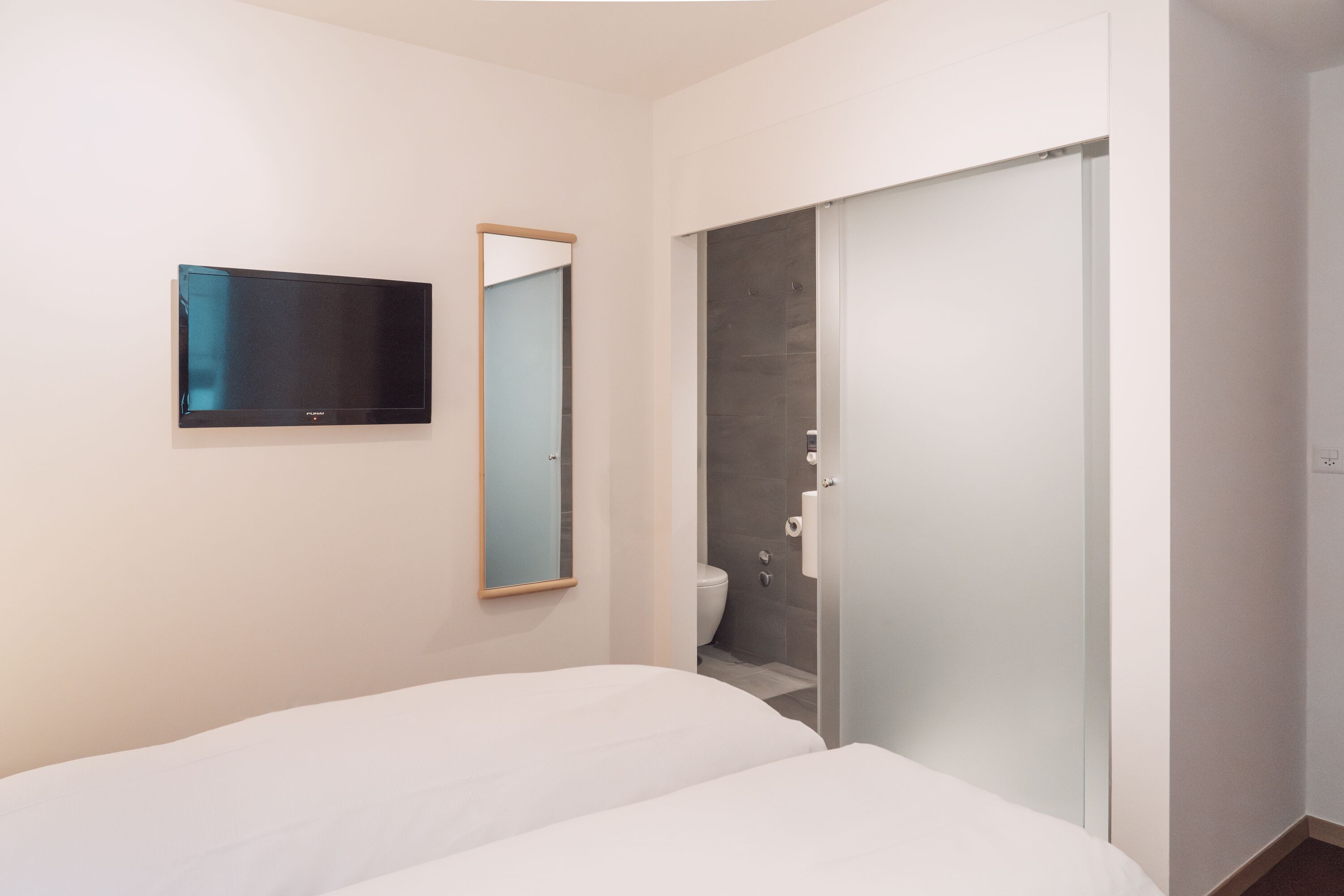 Une chambre d’hôtel moderne équipée d’un lit, d’un téléviseur à écran plat, d’un miroir et d’un espace douche.