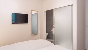 Une chambre d’hôtel moderne équipée d’un lit, d’un téléviseur à écran plat, d’un miroir et d’un espace douche.