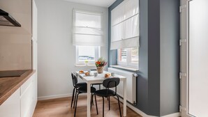 Una cocina moderna con una mesa blanca, sillas negras y un ventanal con persianas blancas.