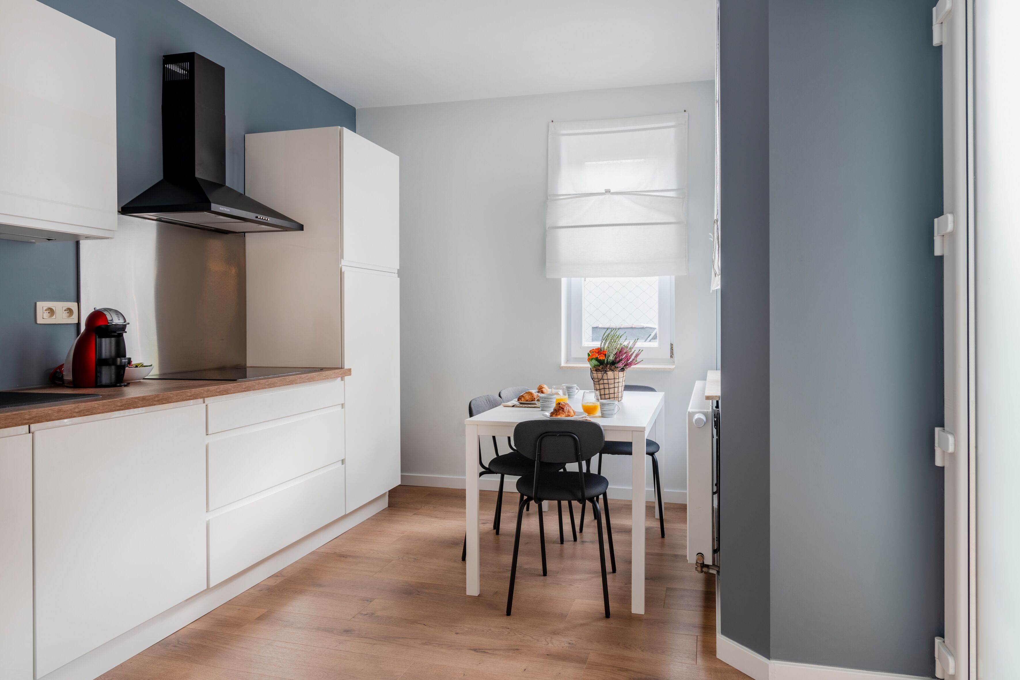 A modern kitchen with white cabinets, a black range hood, and a dining area with a white table and black chairs.