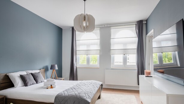 Un dormitorio moderno con una cama grande, mesitas de noche, un aparador y una ventana con cortinas.