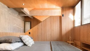 A bedroom with a bed, pillows, a wooden headboard, a small stool, and a window with blinds. - Stylish Roma Norte Loft with Private Terrace (Ciudad de México)