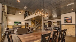 A spacious living area with a large wooden dining table, comfortable seating, a fireplace, and a staircase leading to an upper level.