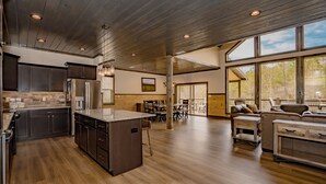 A spacious kitchen with a central island, dark wooden cabinets, and a large window overlooking a forested area.