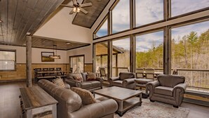 A spacious living room with leather sofas, a coffee table, and a large window offering a view of trees.