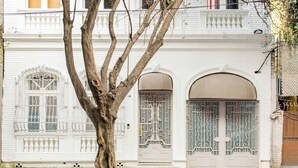 A white building with arched windows and doors, a tree in front, and a fence on the right. - Eco Loft with Terrace Garden & Gym Access (Ciudad de México)