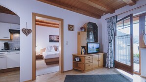 A cozy room with a bed, a TV, and a view of a lake through a window. - Appartement Plattner - TOP 2 (Zell am See)