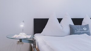 A neatly made bed with white bedding and pillows, a bedside table with a lamp and a magazine, and a framed abstract painting on the wall. - Appartement Plattner - TOP 3 (Zell am See)