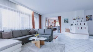 A modern living room with a grey sofa, a round coffee table, and a dining area in the background. - Appartement Plattner - TOP 3 (Zell am See)