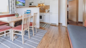 Een gezellige, kleine keuken met een magnetron, kookplaat en spoelbak. Er is een eethoek met een tafel en stoelen, en een bank in de hoek.