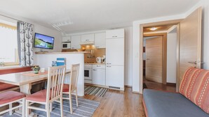 Een ruimtelijk ingerichte leefruimte met een kitchenette, eethoek en een slaapbank.