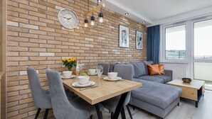 A modern living room with a brick wall, a dining table set with plates and glasses, a grey sofa, and a small side table. - Seaside Apartamenty Platany Kołobrzeg  (Kolobrzeg)
