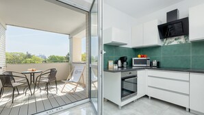 A modern kitchen with a microwave, oven, and a dining area with chairs and a table. - Seaside Apartamenty Platany Kołobrzeg  (Kolobrzeg)