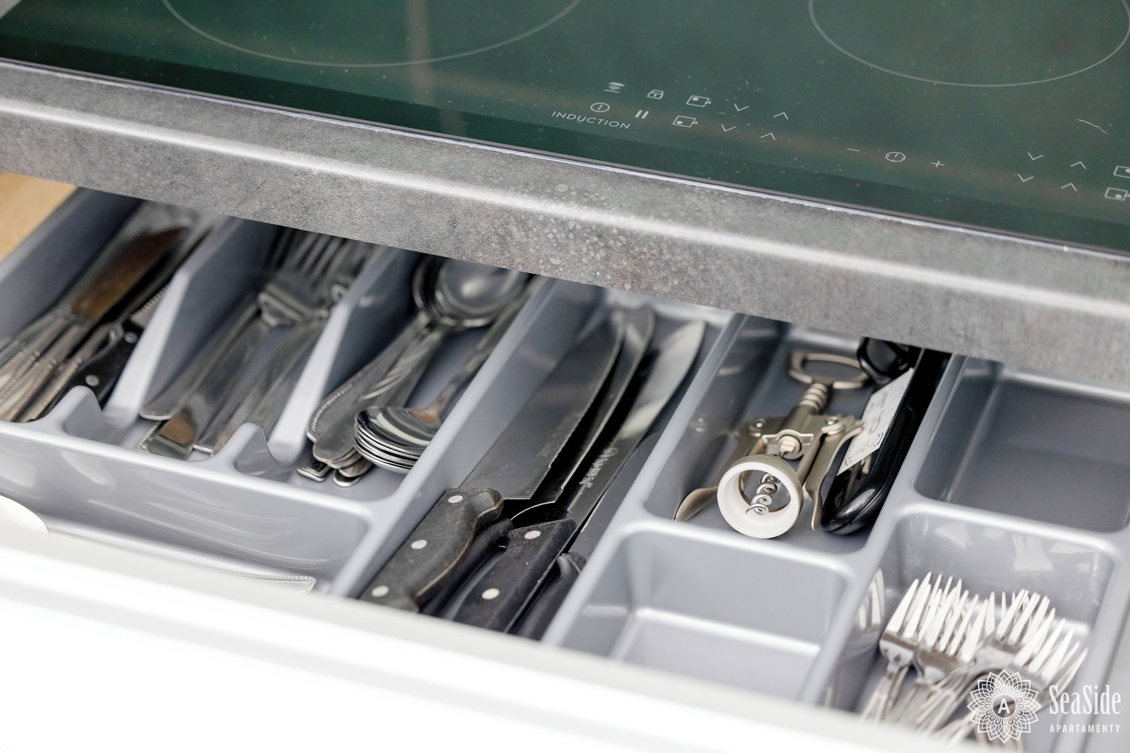 A drawer with utensils and a can opener.
