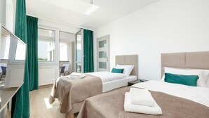 A hotel room with two beds, a window with curtains, a radiator, and a view of the outside. - Seaside Apartamenty Platany Kołobrzeg  (Kolobrzeg)