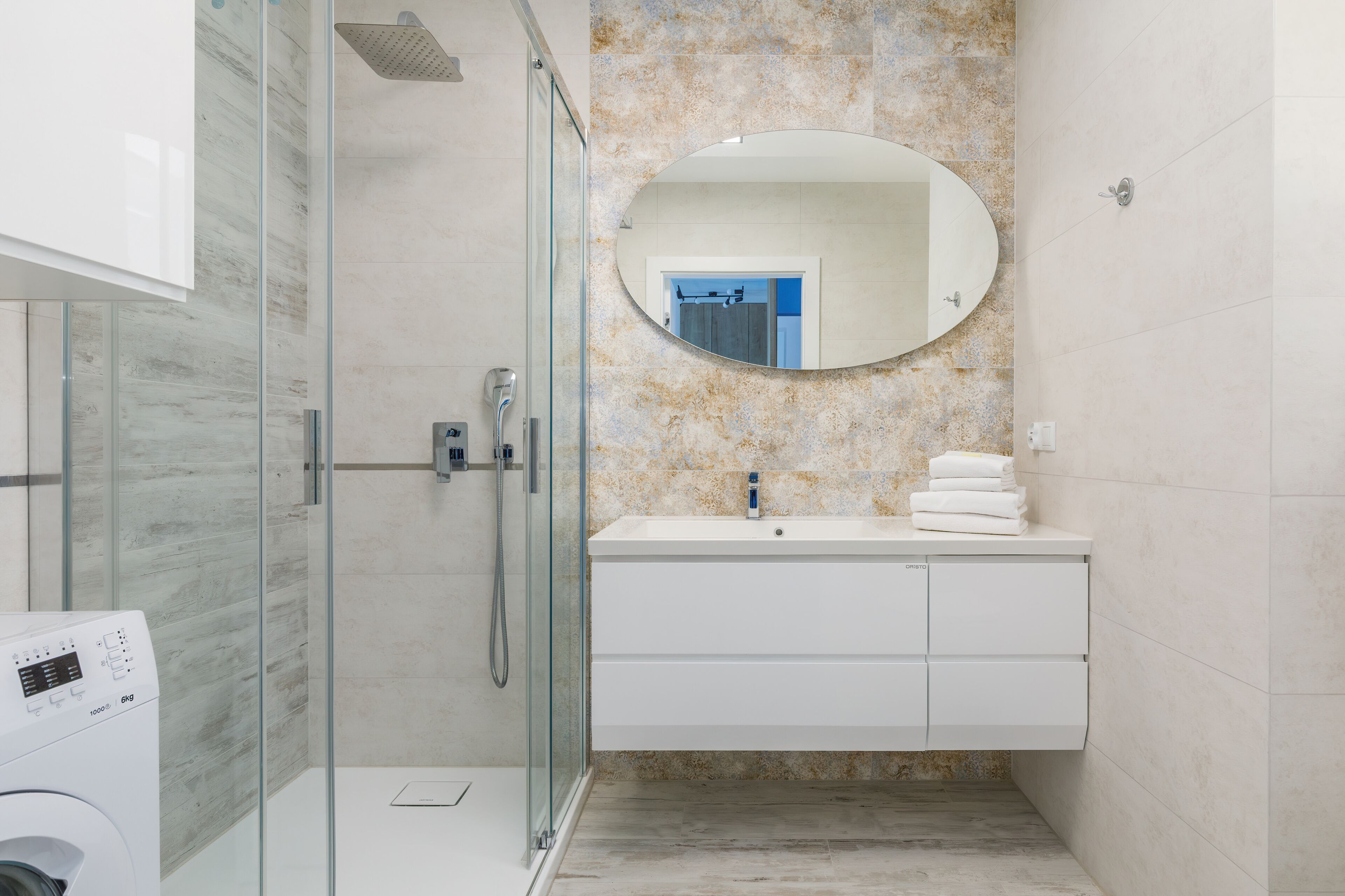 Uma casa de banho moderna com chuveiro com divisória de vidro, um lavatório branco com um espelho grande e parede com padrão marmorizado.