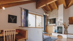 A cozy living room with a wooden ceiling, a stone wall, a fireplace, and a television. - Appartement Haus Elise - TOP 3, balcony & mountain view (Zell am See)