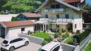 A two-story house with a balcony, a covered patio, and a driveway with two cars. - Appartement Haus Elise - TOP 3, balcony & mountain view (Zell am See)