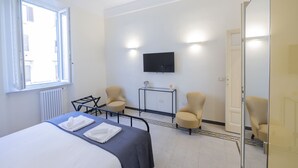 Ett hotellrum med en säng, två fåtöljer, ett litet bord, en tv som är monterad på väggen och en dörr med en spegel.